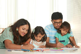 A family of four--two adults and two young school-age children, sit together coloring.