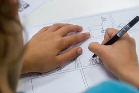 Bird's eye view of a children creating a comic page using a pen.