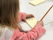 side view of a child writing on an index card with a pencil.